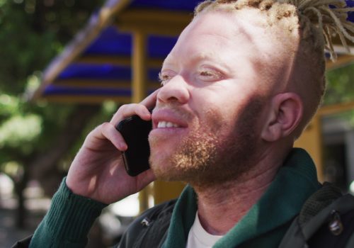 happy-albino-african-american-man-with-dreadlocks-in-park-talking-on-smartphone-SBI-350723777 (1)